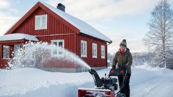 Person bruker snøfreser for å rydde innkjørselen foran et norsk hus om vinteren